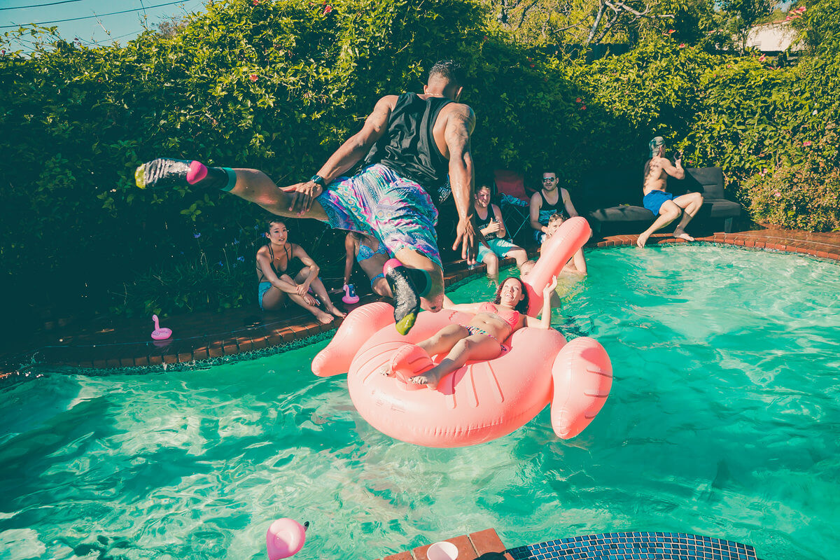 Guy jumping in a pool during a pool party. Fun and young people enjoying summer and the heat